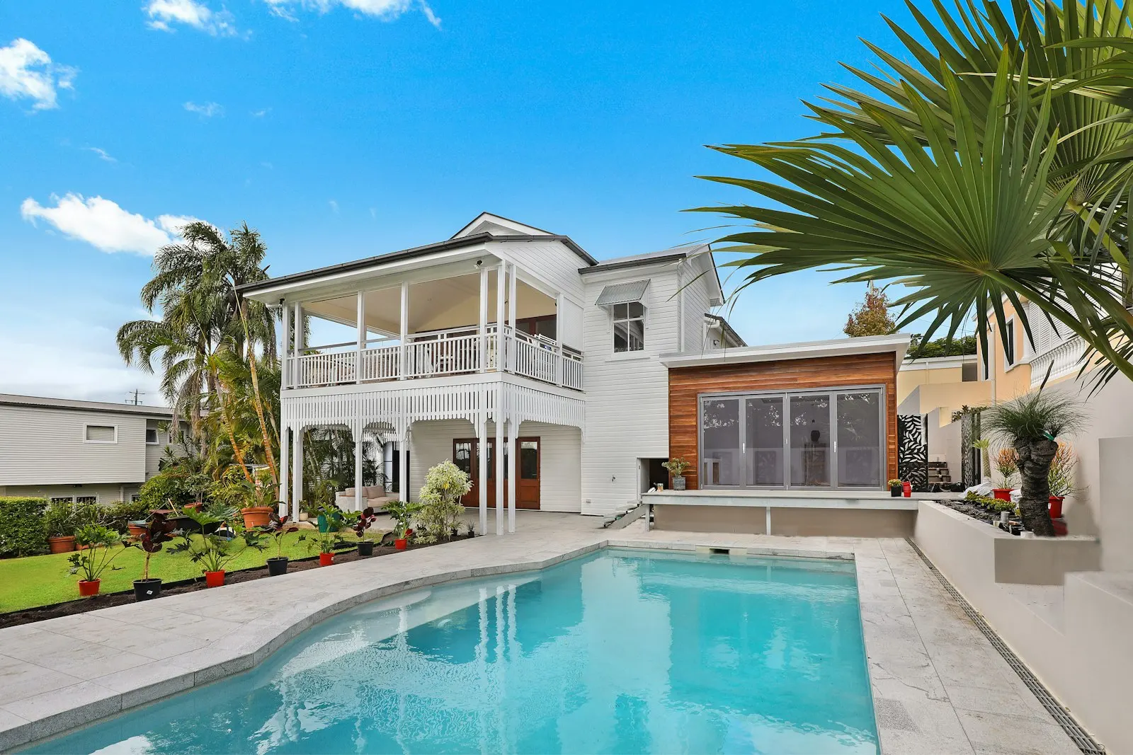 White two story house with a balcony, palm trees, and a swimming pool